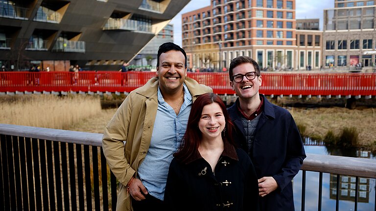 Lib Dem candidates for Rotherhithe, Vikas, Sorcha and JK, stand on a bridge over Canada Water with the Library and high rise flats in the background